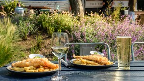 A table with plates of fish and chips, a glass of beer, and a glass of white wine. - The Ship at Dunwich (Saxmundham)
