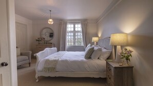 A bedroom with a large bed, a bedside table with a lamp, a dresser, a chair, a mirror, and a window with curtains. - The Ship at Dunwich (Saxmundham)