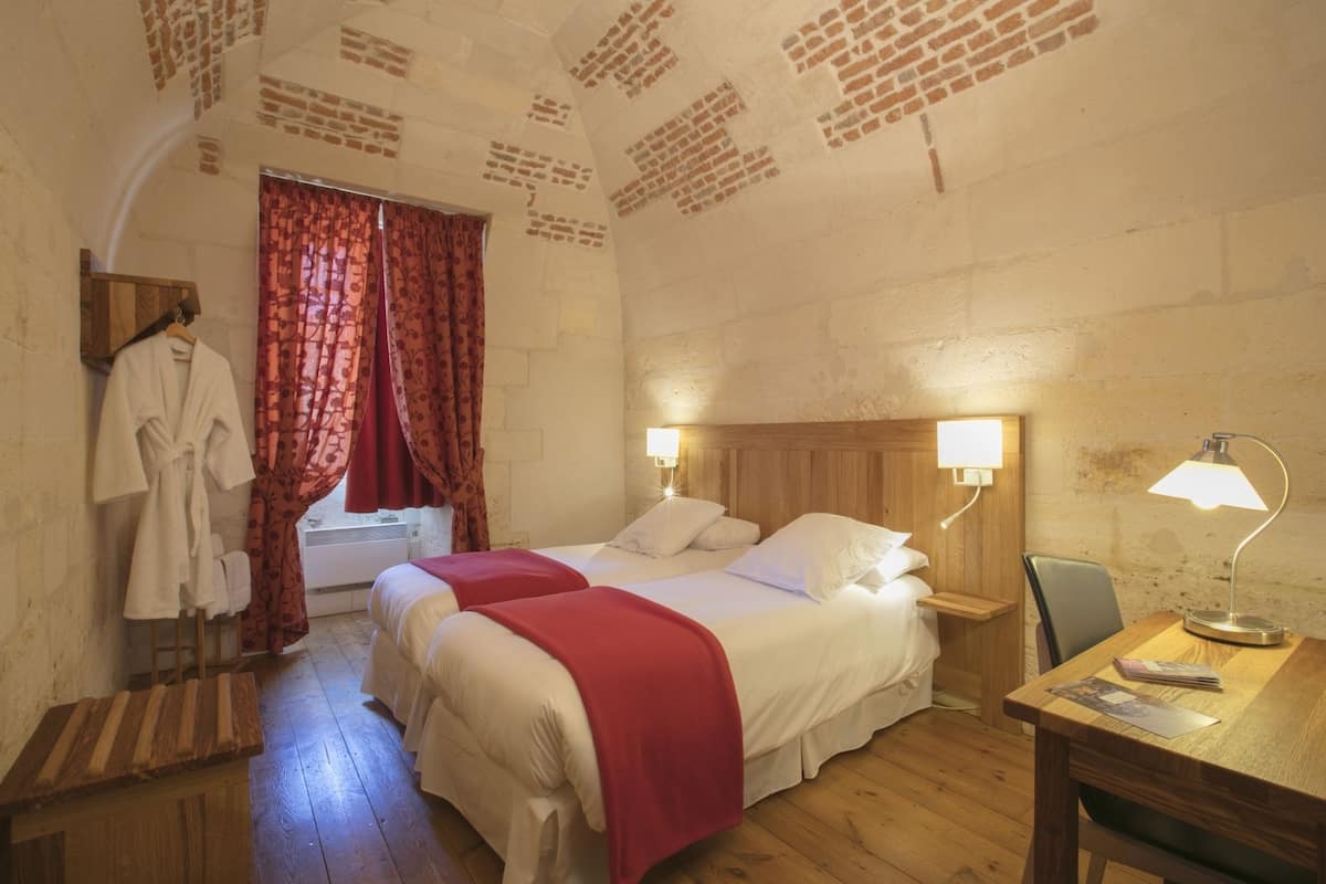 Une chambre avec deux lits, un bureau en bois, une chaise, un peignoir et une fenêtre avec des rideaux.
