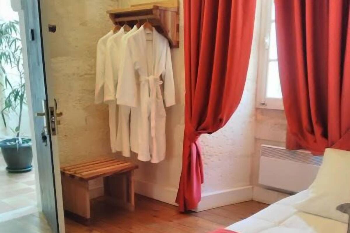Une chambre à coucher comprenant un lit, un banc, un portant à vêtements et une fenêtre avec des rideaux.