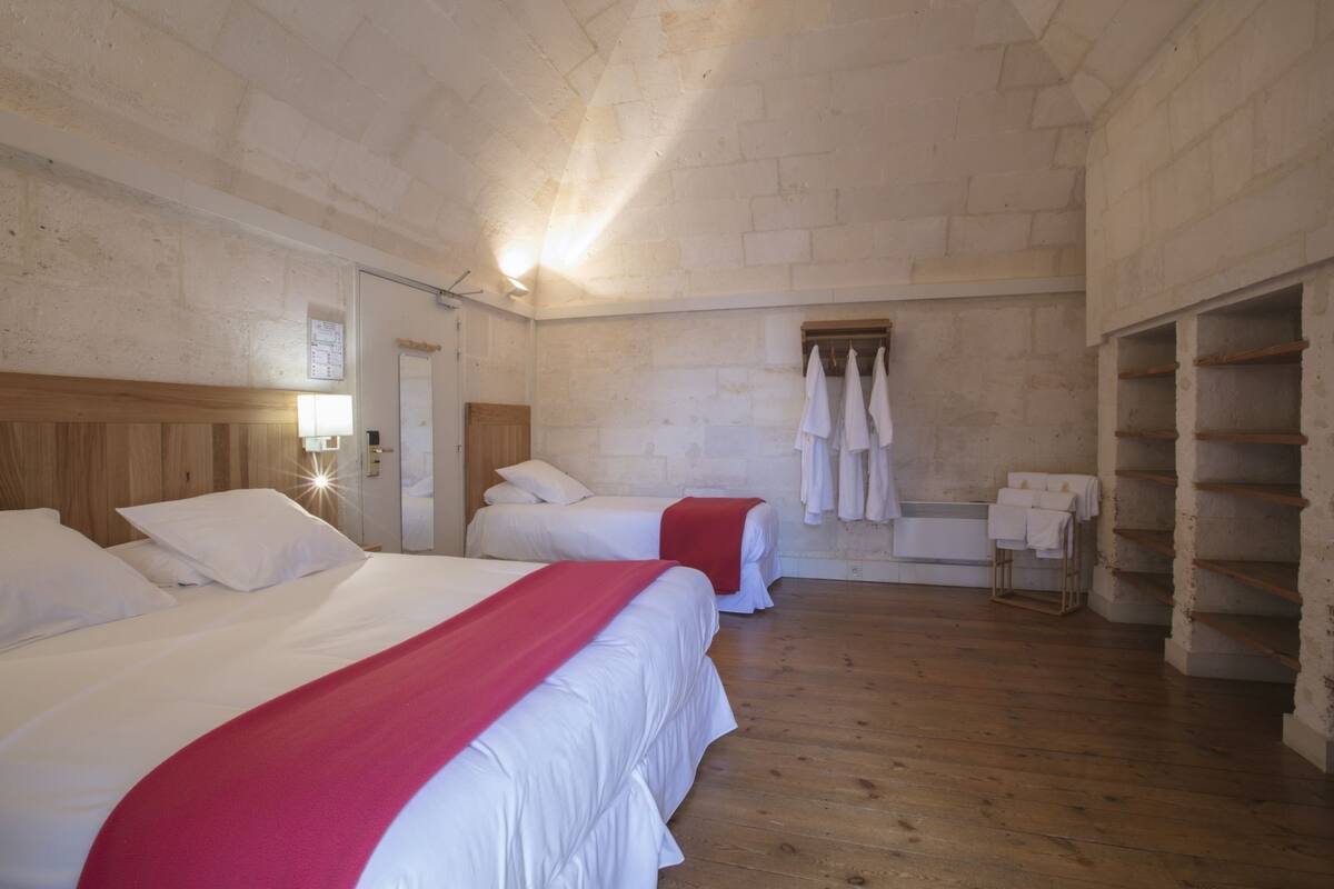 Une chambre avec deux lits, un plancher en bois, des murs en pierre, un miroir et un porte-serviettes.