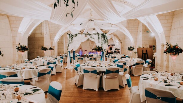 Un salón de banquetes con mesas redondas, manteles blancos y cintas azules en las sillas.