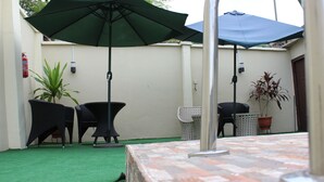 Un espacio al aire libre con un patio, dos sillas negras, una mesa y dos sombrillas.