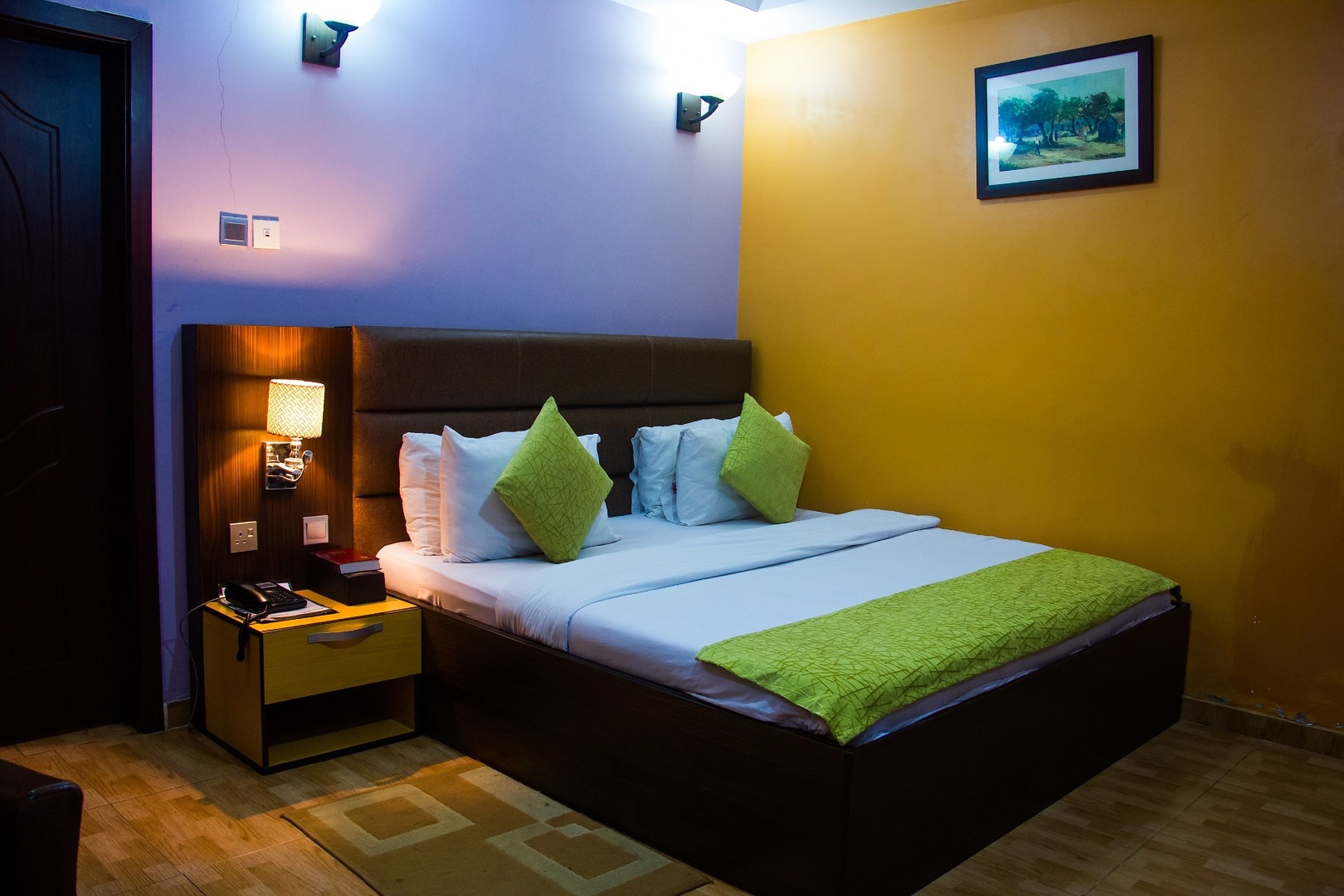 A neatly made bed with a green throw, a bedside lamp, and a nightstand with a phone and a book.