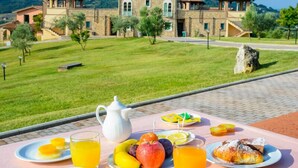 A breakfast setup with fruit, juice, and pastries on a table overlooking a stone building with a garden. - Pian Dei Mucini Resort Le Ville (Massa Marittima)