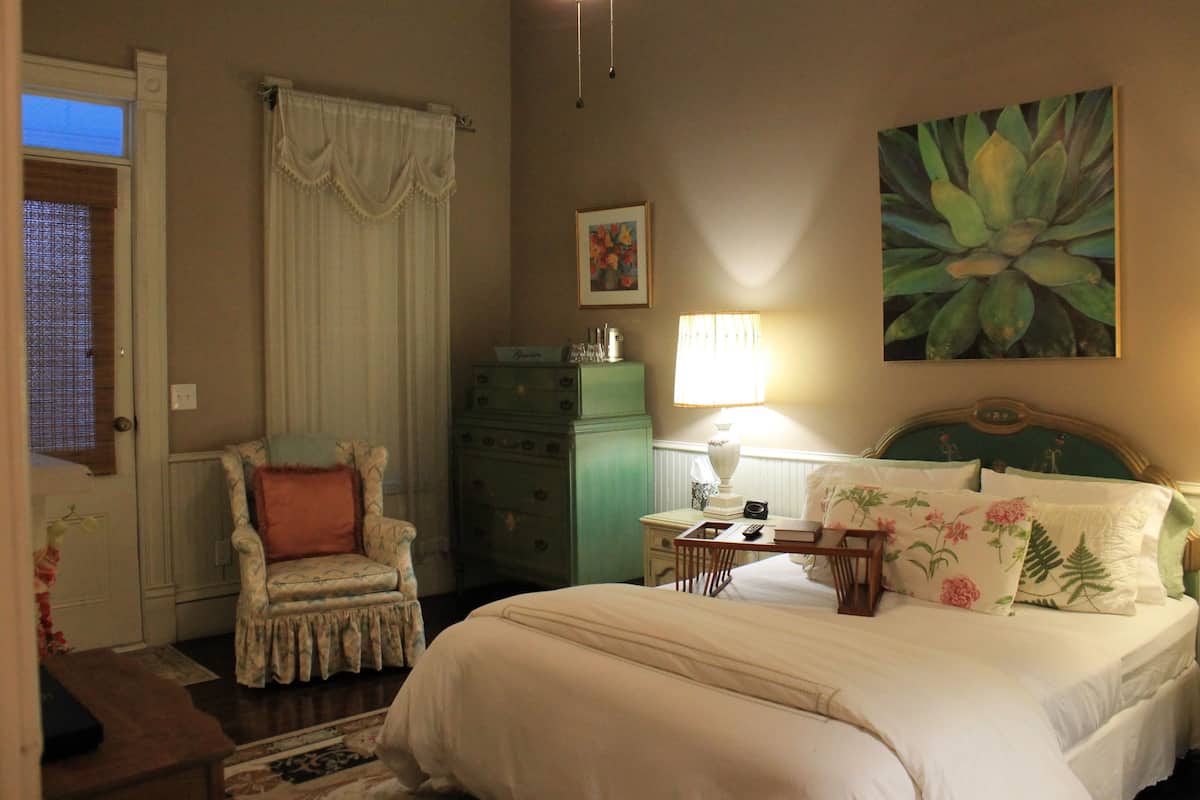 A bedroom with a bed, a chair, a dresser, a lamp, and a painting on the wall.