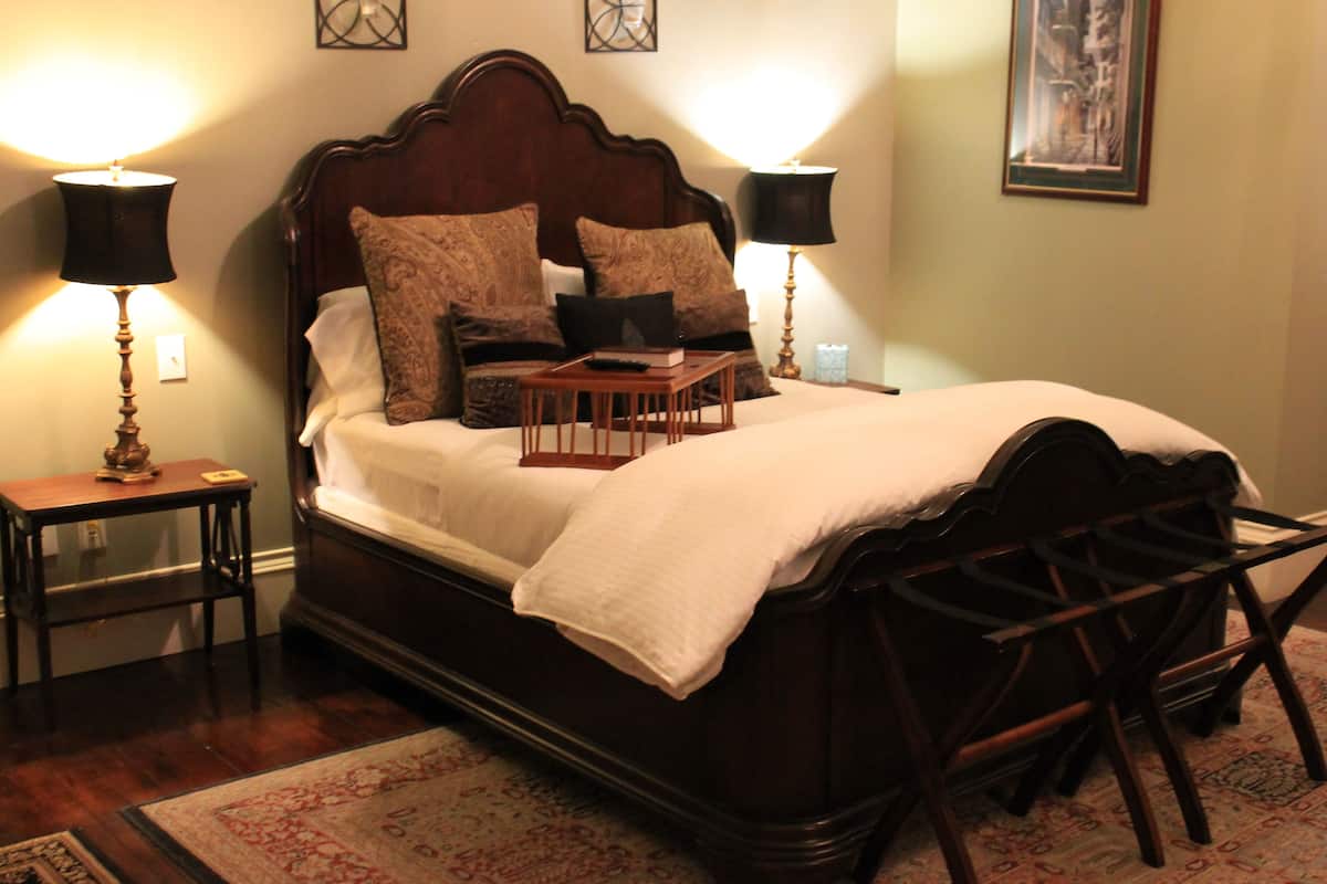 A neatly made bed with a wooden headboard, two bedside tables with lamps, and a patterned rug on the floor.