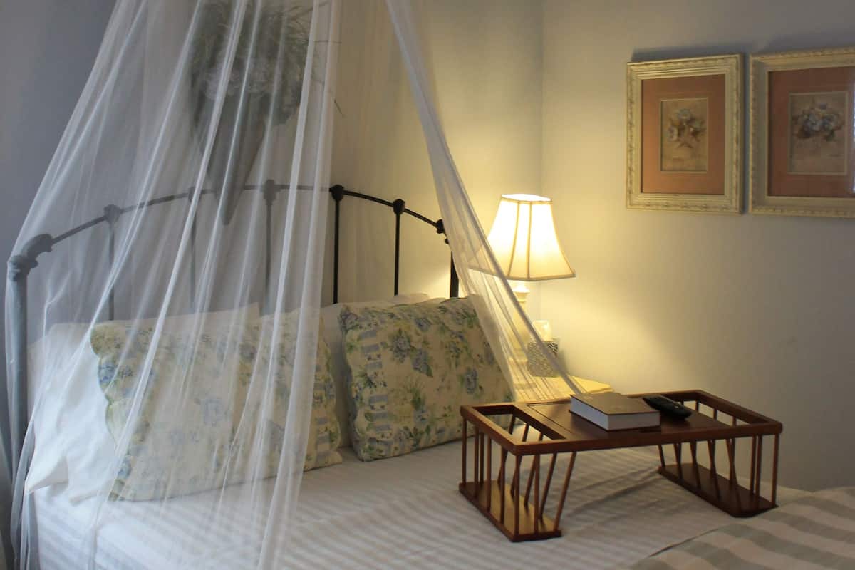 A bedroom with a canopy bed, a bedside table with a lamp, and two framed pictures on the wall.