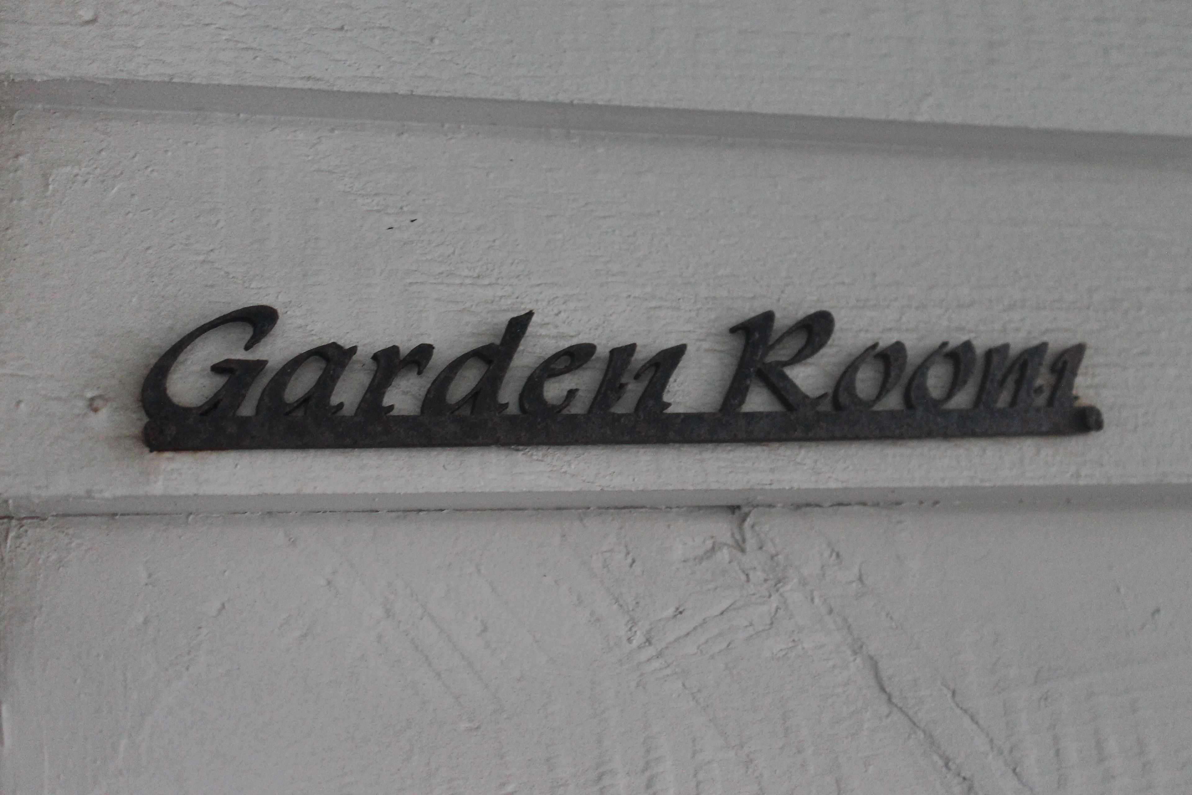 A metal sign with the words "Garden Room" on a white wall.