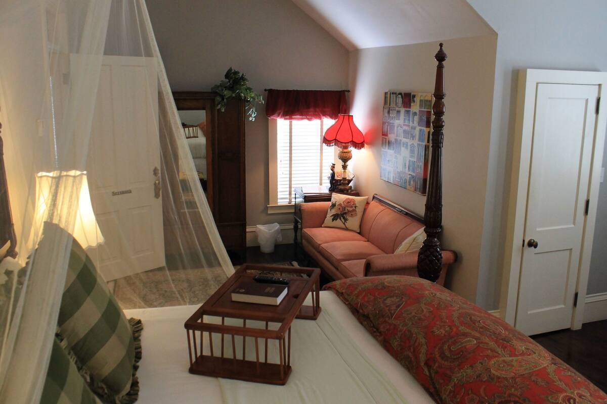 A bedroom with a canopy bed, a sofa, a coffee table, a lamp, and a door.