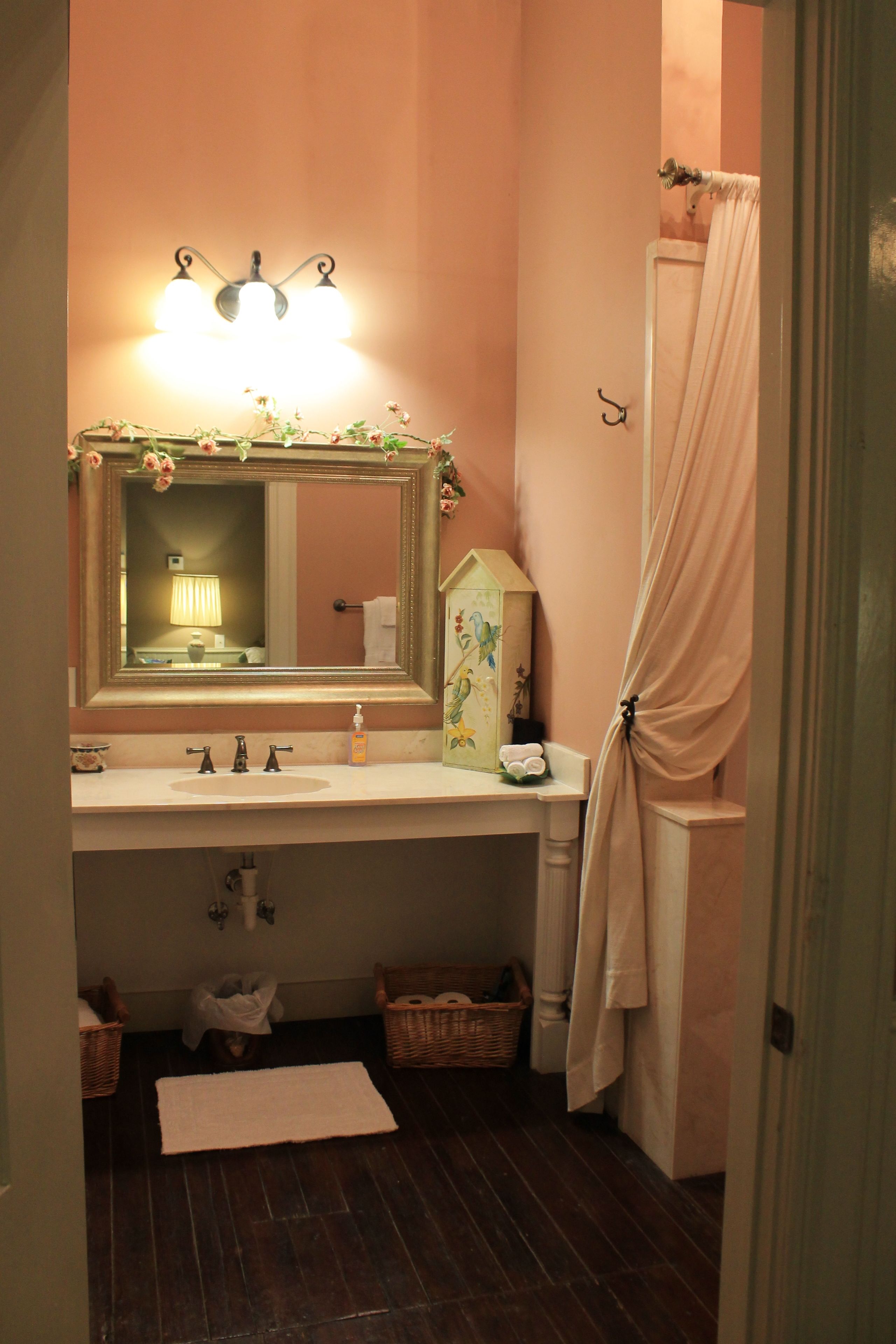 A bathroom with a vanity, a mirror, a towel rack, a shower curtain, and a small decorative house.