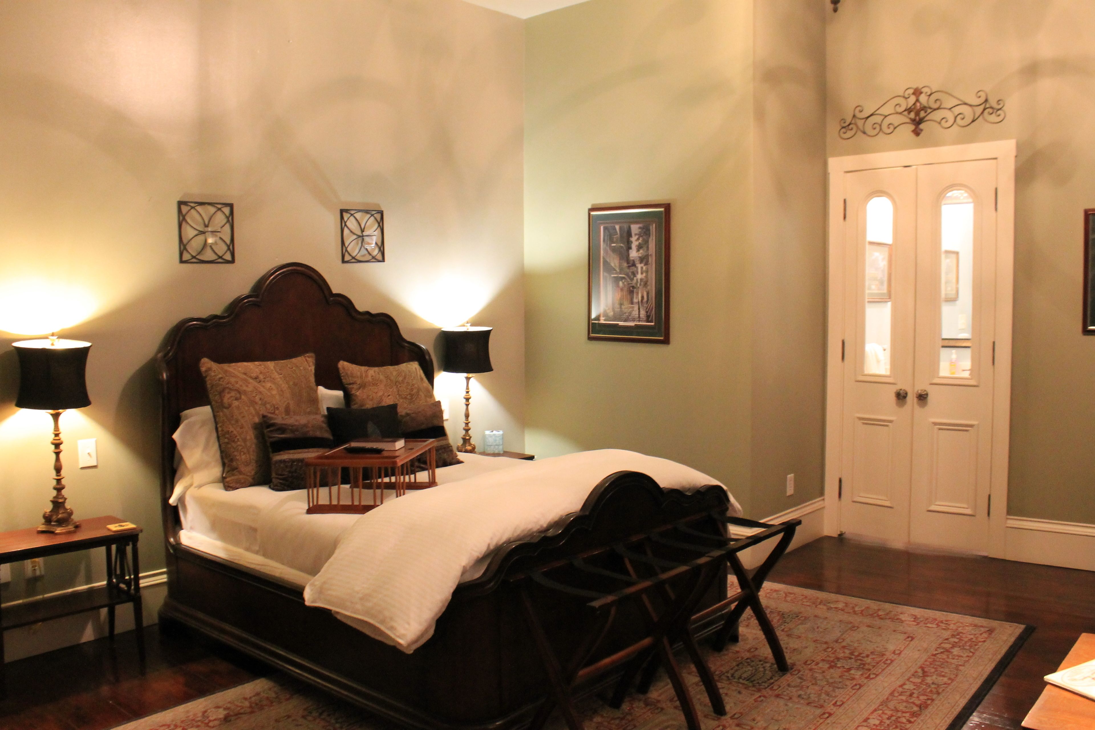 A neatly arranged bedroom with a large bed, bedside lamps, a nightstand, and a door with a mirror.