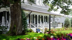 En vit byggnad med en veranda, en skylt med texten ”Grand Magnolia Suites and Ballrooms”, och en trädgård med färgstarka blommor.