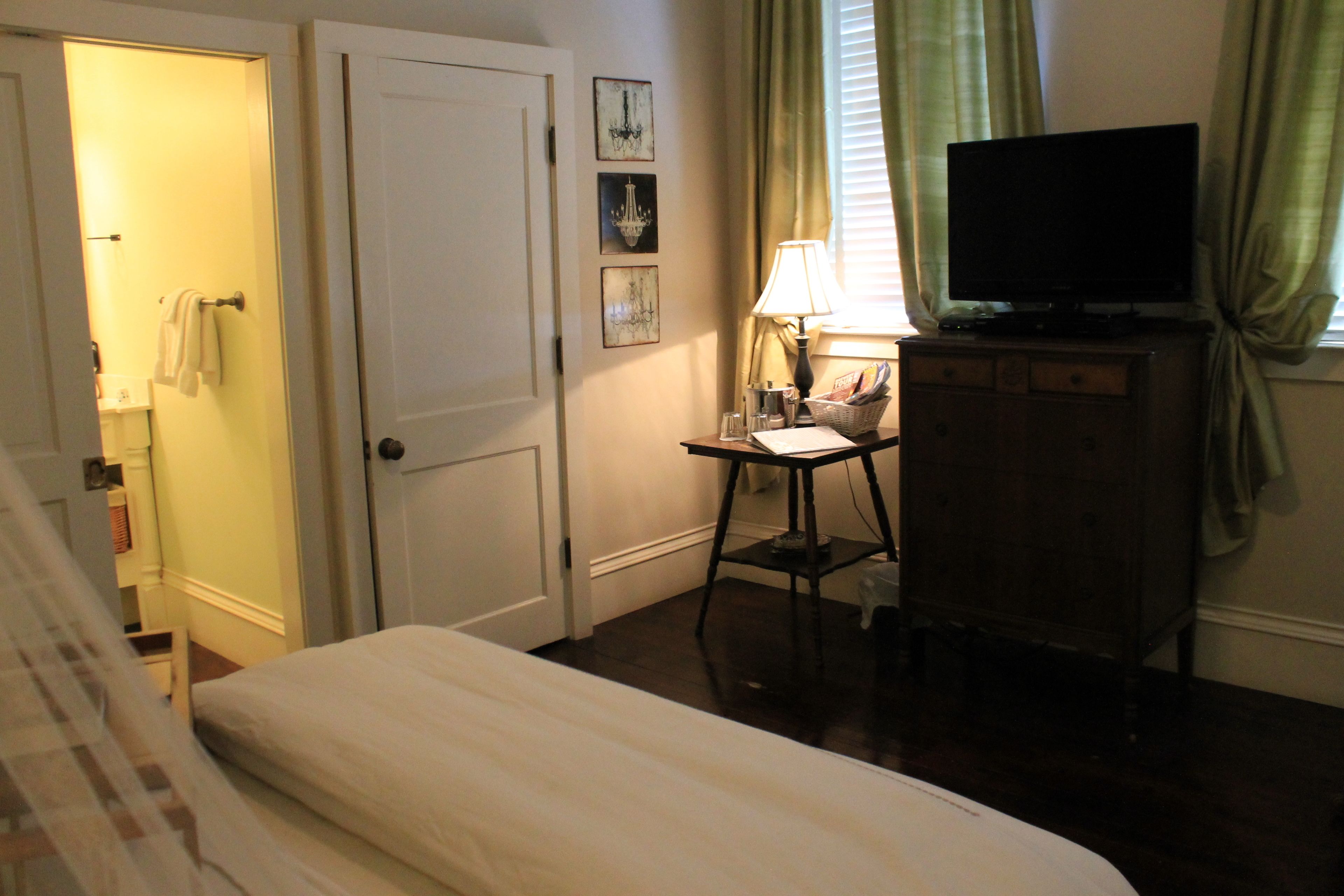 Un dormitorio con una cama, un escritorio con lámpara, un televisor y una puerta que da a un baño.