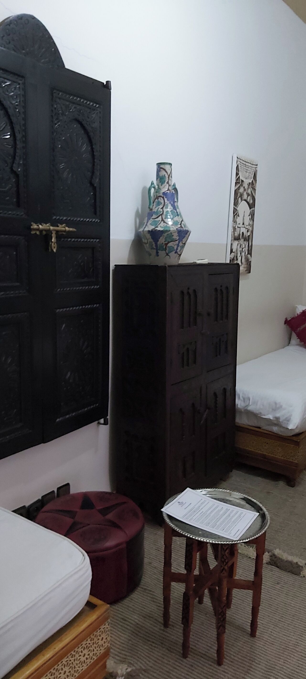 Una habitación con una cama, un armario de madera, un taburete pequeño y una puerta negra.