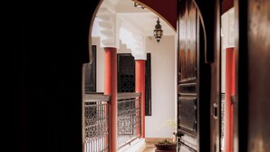A corridor with a tiled floor, a large potted plant, and a black door. - Riad Ajebel (Marrakech)