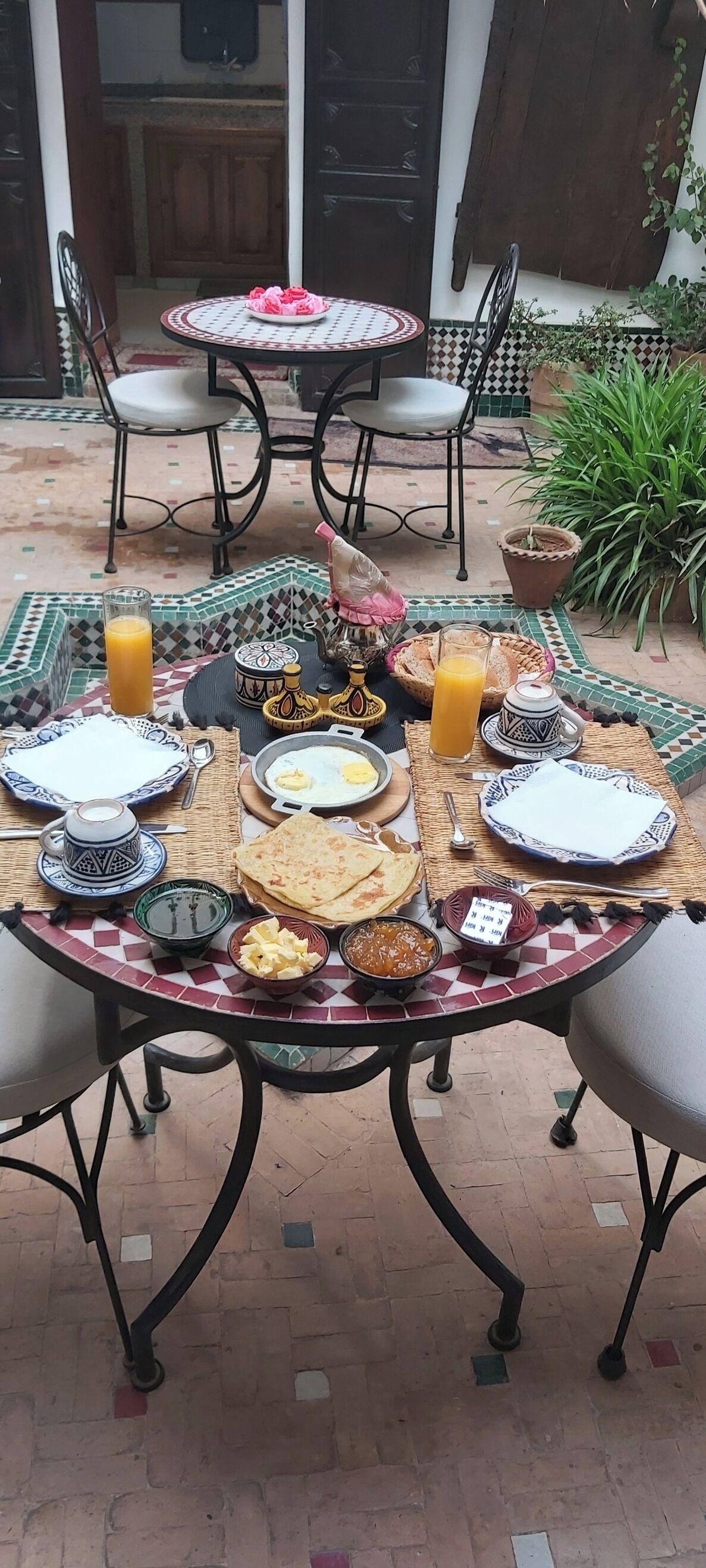 Una mesa de comedor dispuesta con diferentes platos, un vaso de jugo de naranja y una taza de té.