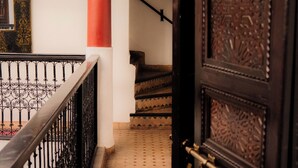 A staircase with ornate metal railings and a patterned floor leading to a room with a large, intricately designed door. - Riad Ajebel (Marrakech)
