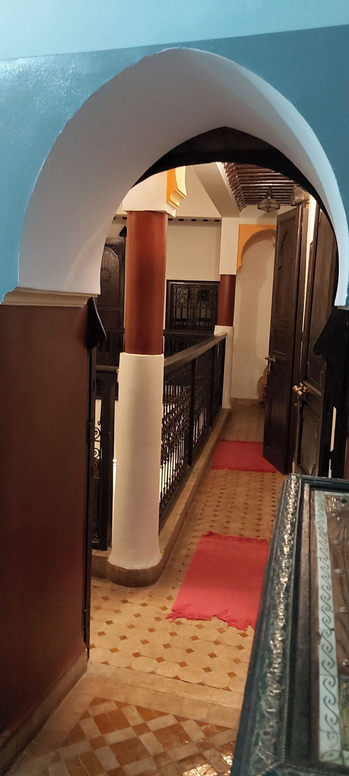 A corridor with a checkered floor, a red carpet, and a white archway.
