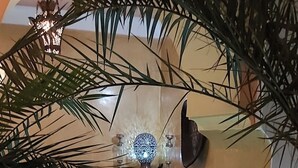 An indoor swimming pool with a tiled border, surrounded by palm trees and a decorative wall. - Riad Ajebel (Marrakech)