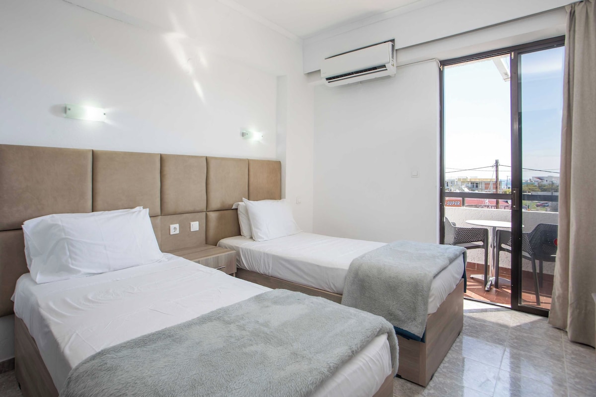 Ein Hotelzimmer mit zwei Betten, einem Balkon mit Tisch und Stühlen sowie einer Klimaanlage.