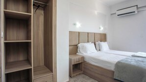 Quarto com guarda-roupa de madeira, mesa de cabeceira, cama com roupa de cama branca e unidade de ar condicionado na parede.