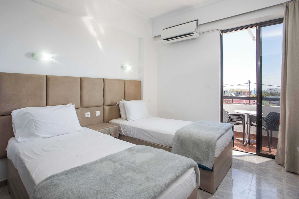 Ein Hotelzimmer mit zwei Betten, einem Balkon mit Tisch und Stühlen sowie einer Klimaanlage.