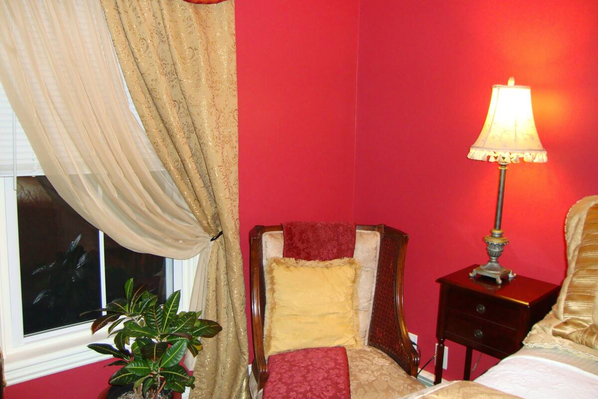 A room with a bed, a nightstand, a lamp, a window with curtains, and a potted plant.