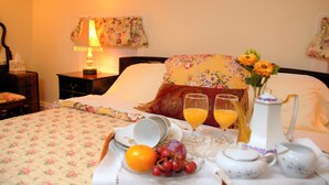 Una cama bien hecha con ropa de cama floral, una mesita de noche con lámpara y una bandeja de desayuno con frutas y una jarrón.