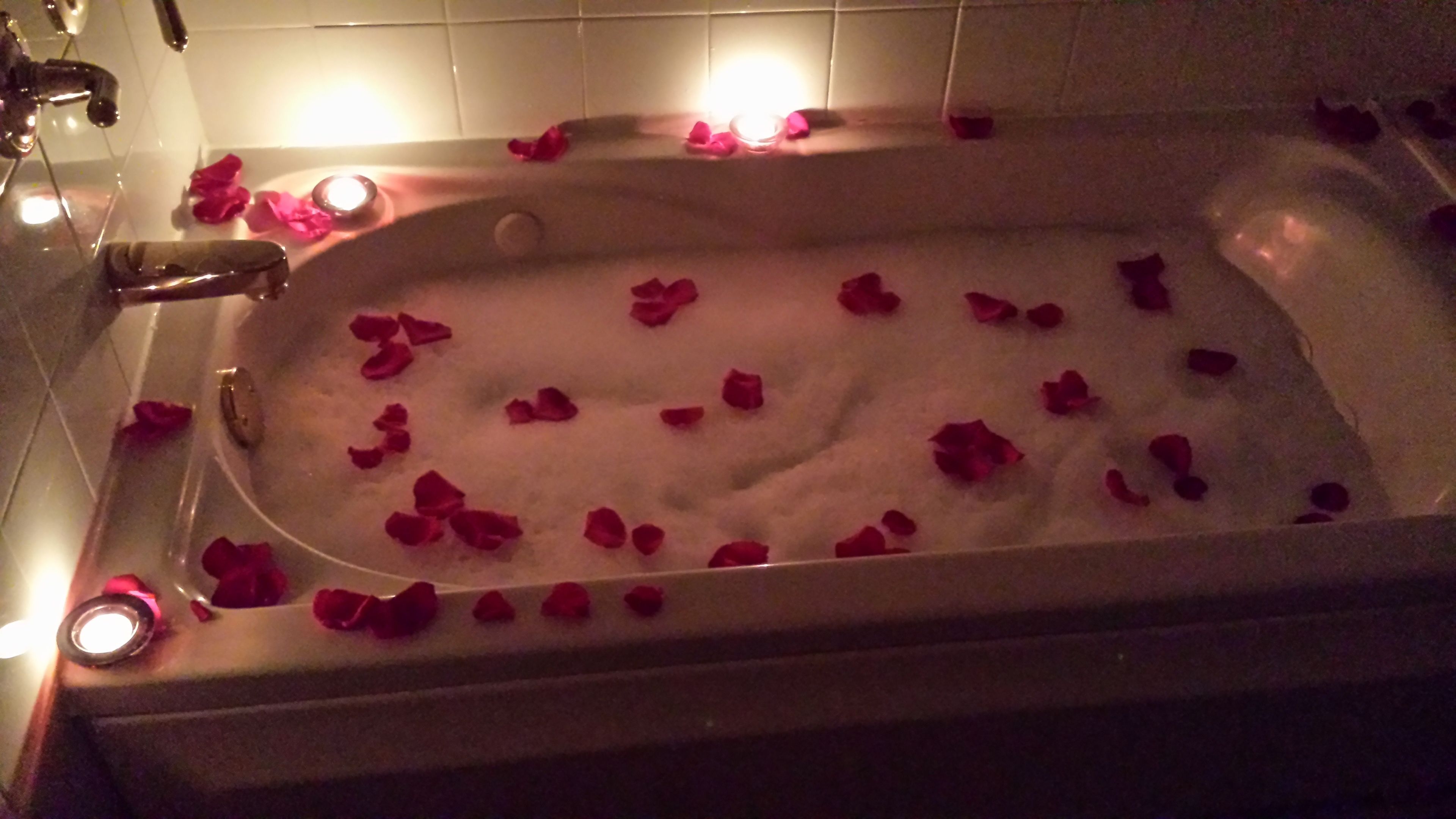 A bathtub filled with water and rose petals.