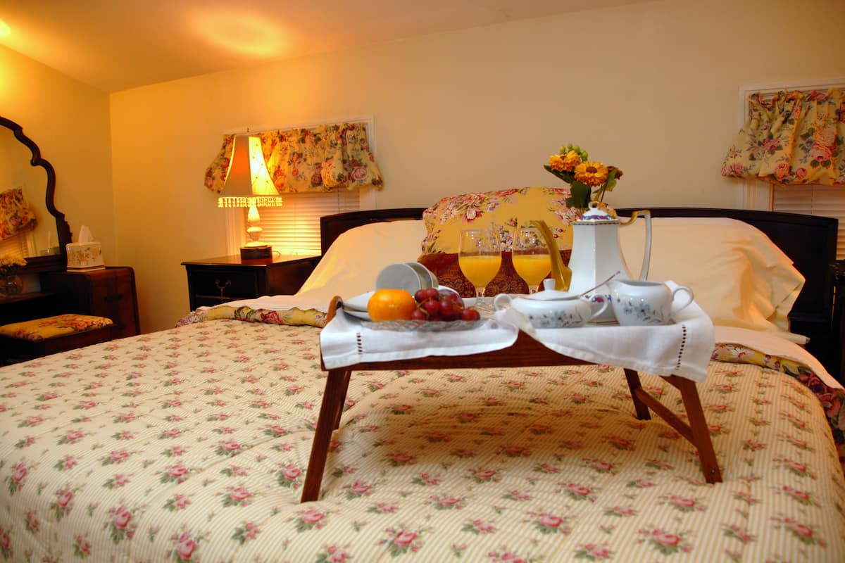 A neatly made bed with a floral bedspread, a bedside table with a lamp, and a tray with fruits and a pitcher of orange juice.