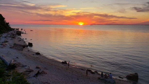 Una playa con un atardecer, agua tranquila y rocas dispersas.