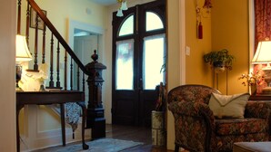 Una escalera de madera con una lámpara, un sillón floral y un ventanal con cortinas.