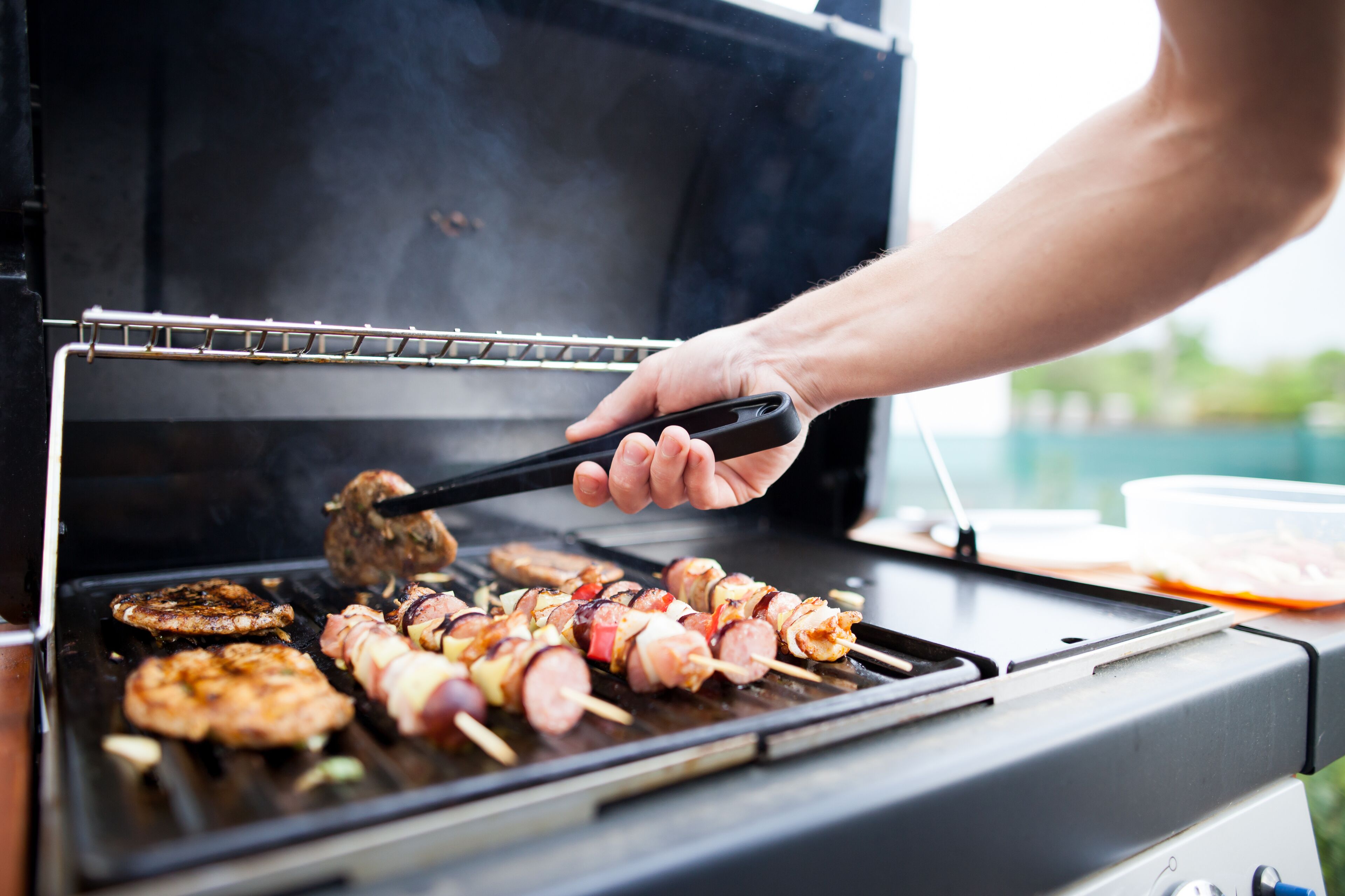 A person grilling various meats and vegetables on an outdoor grill.