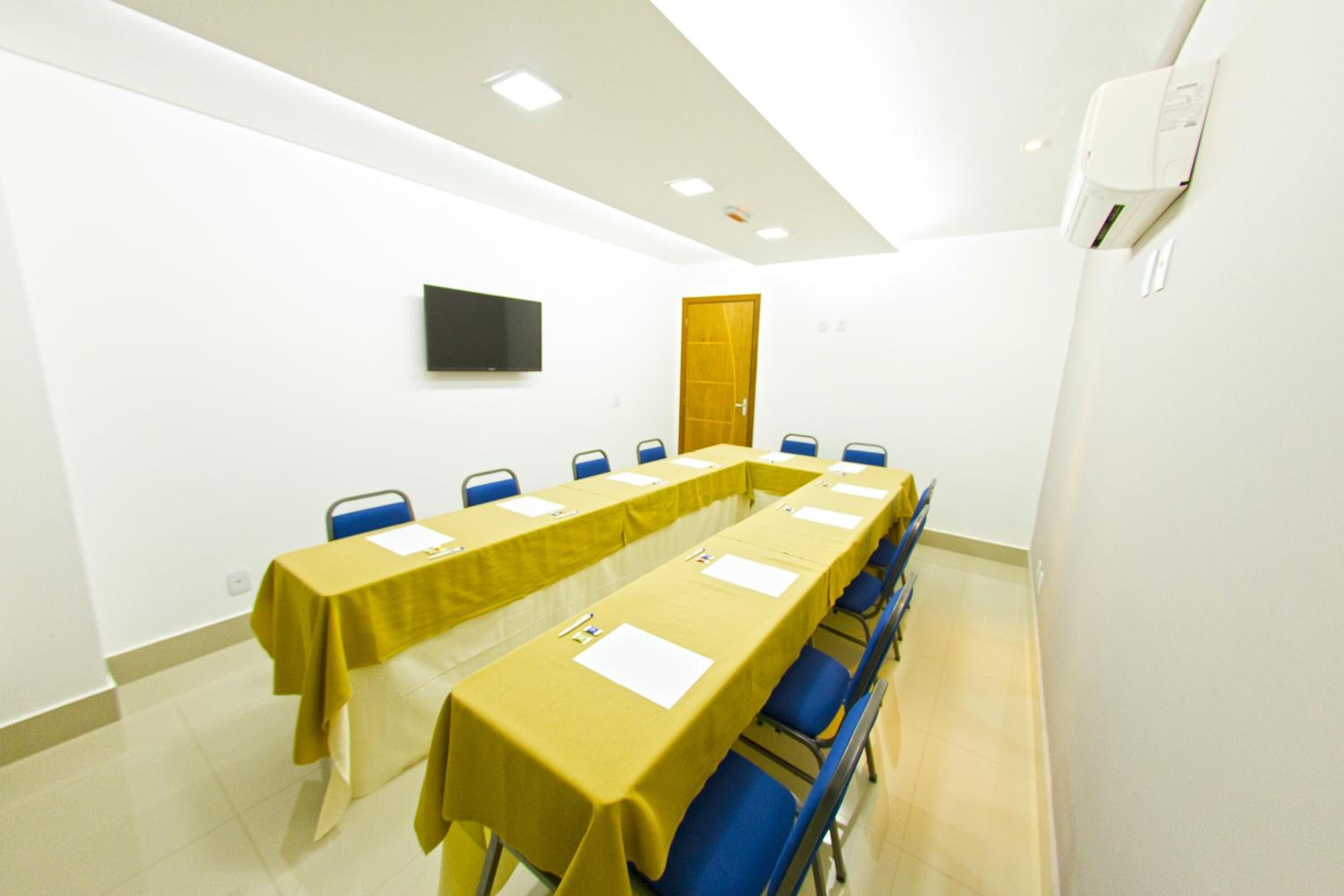 A conference room with a long table, blue chairs, and a flat-screen TV on the wall.