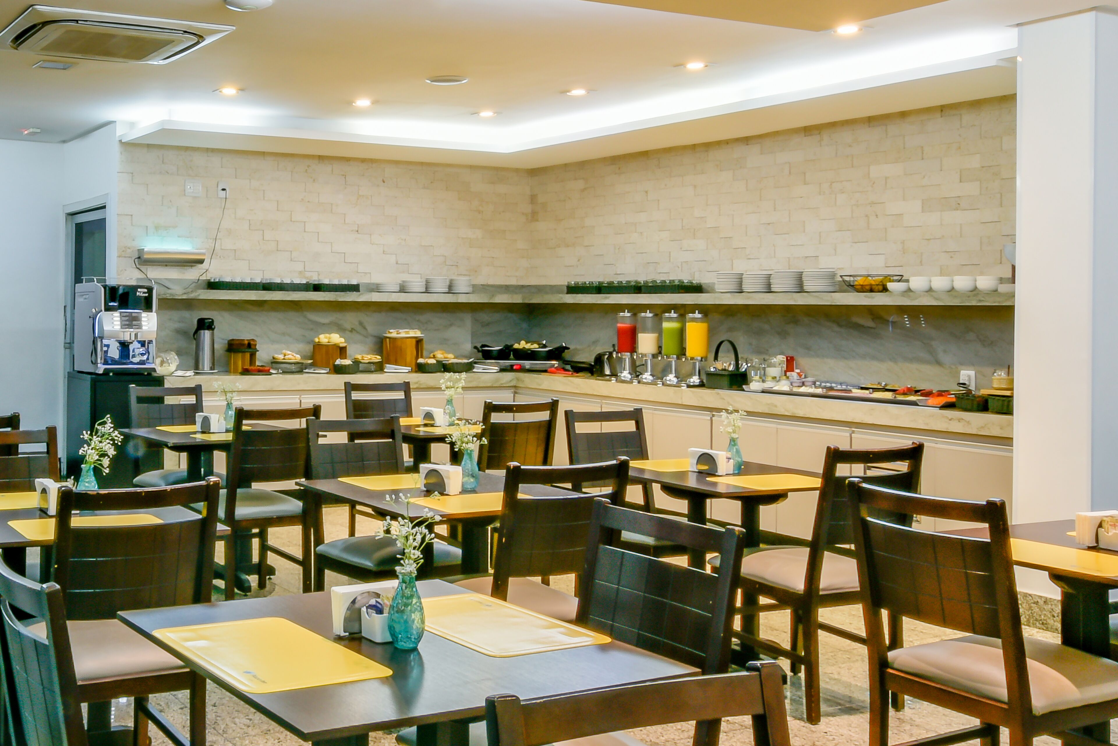 A restaurant with multiple tables and chairs, a kitchen area with various appliances and food items, and a brick wall.