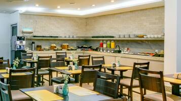 Un restaurant doté de nombreuses tables et chaises, d’une cuisine équipée de divers appareils et contenant différents produits alimentaires, et d’un mur en briques.