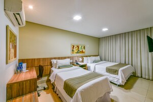 A hotel room with two beds, a desk, a chair, an air conditioner, and a painting on the wall.