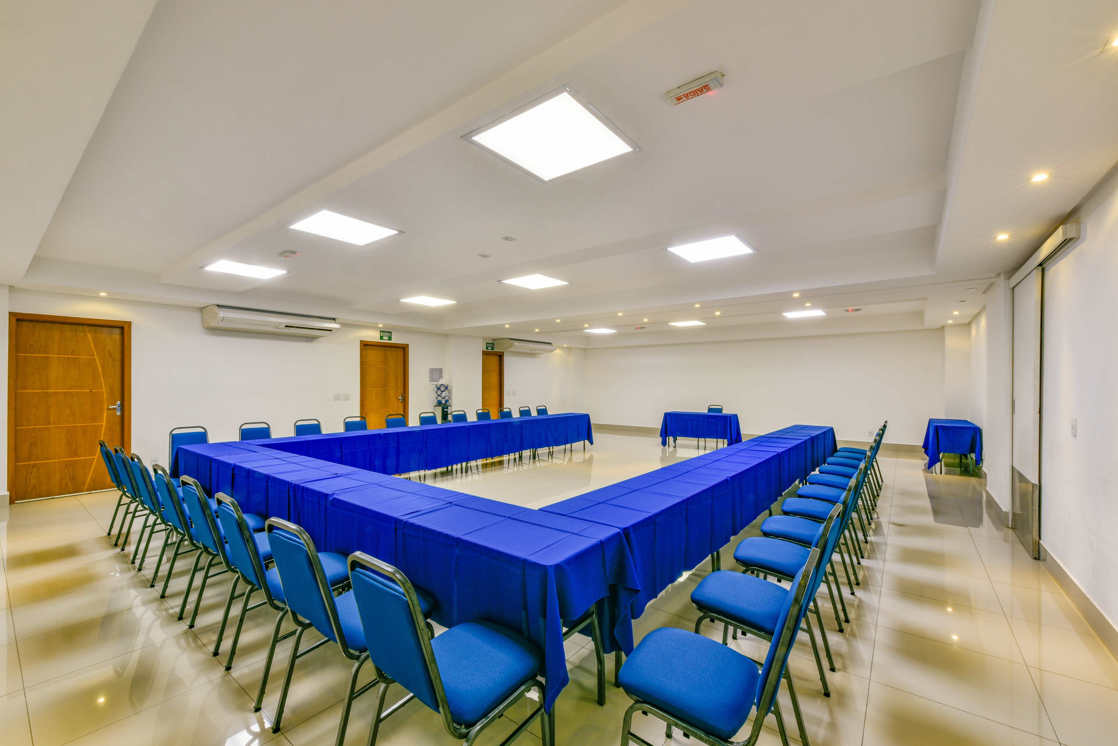 Ein Konferenzraum mit langem Tisch und blauen Stühlen, weißen Wänden und Deckenleuchten.