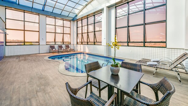 A spacious indoor pool area with a glass ceiling, a pool table, and wicker chairs. - Plaza Inn Breeze Aeroporto (Goiania)