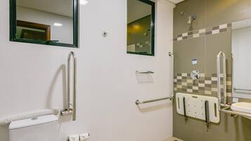 Un baño con inodoro, bidé, barras de apoyo y un espejo.
