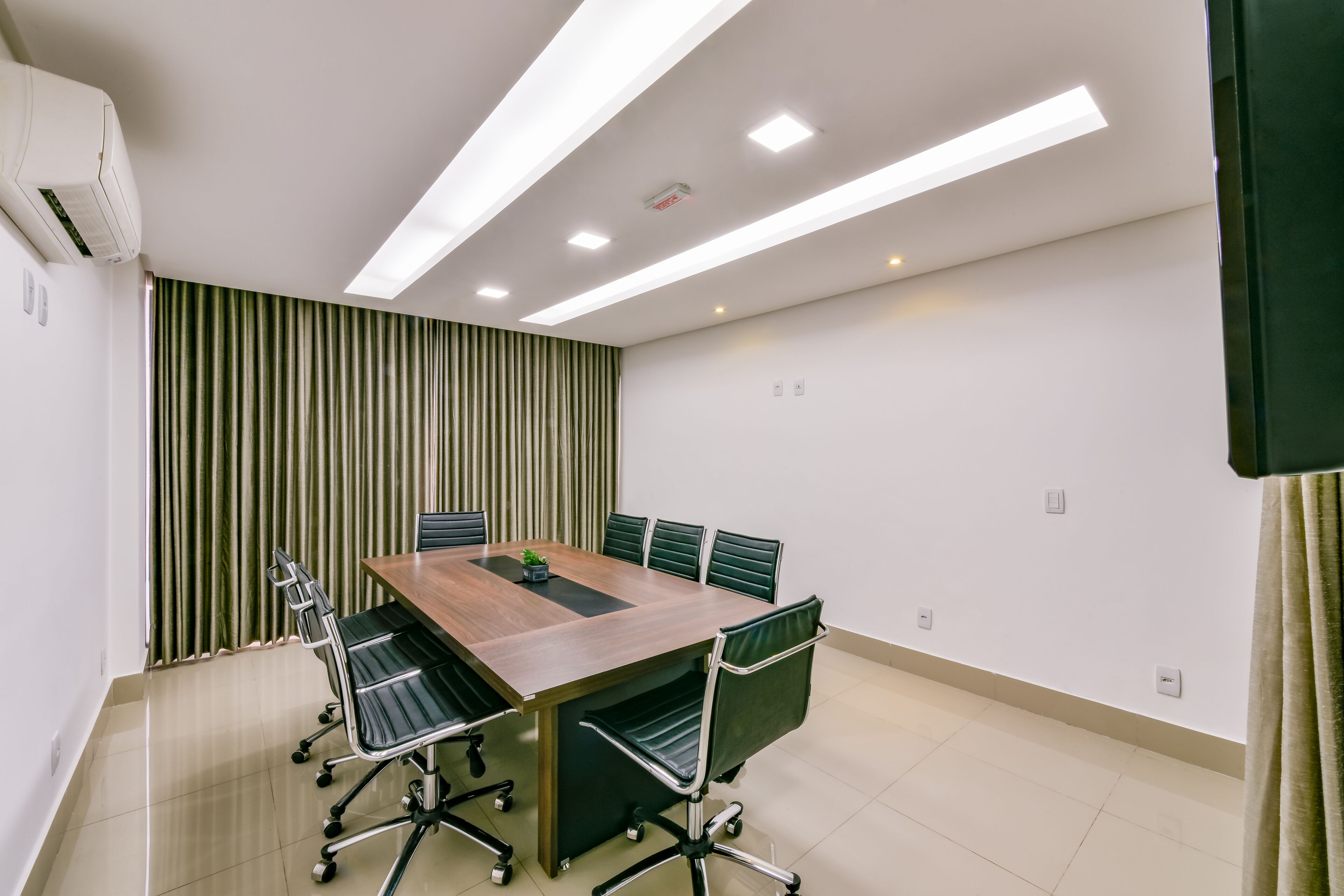 A conference room with a wooden table, black chairs, and a green curtain backdrop.