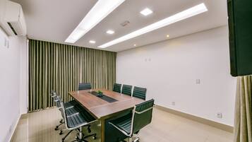 A conference room with a wooden table, black chairs, and a green curtain backdrop.