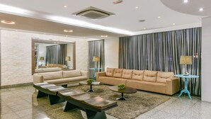 A modern living room with a beige sofa, two coffee tables, and a large mirror. - Plaza Inn Breeze Aeroporto (Goiania)