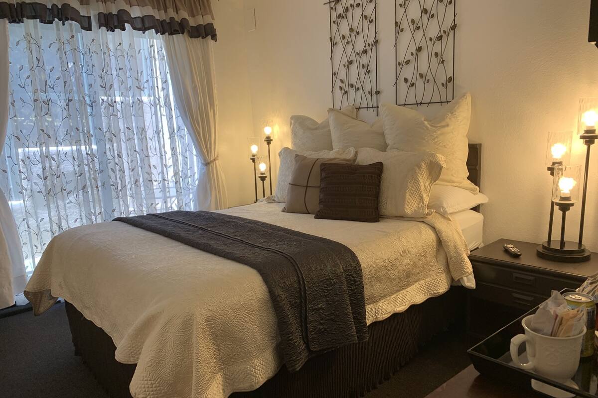 Ein ordentlich gemachtes Bett mit weißer und brauner Decke, ein Nachttisch mit Fernbedienung und eine Nachttischlampe.