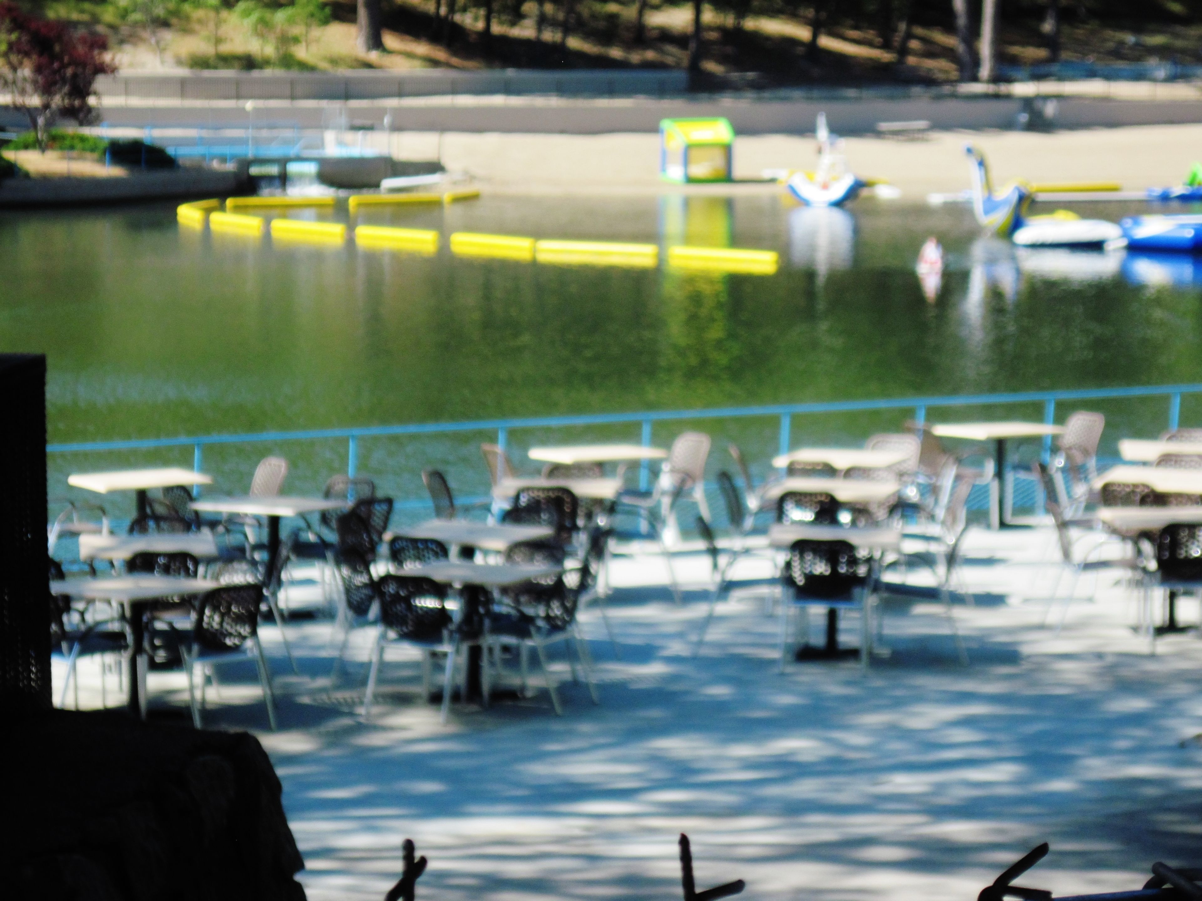 A lakeside patio with tables and chairs, boats on the water, and a fence.