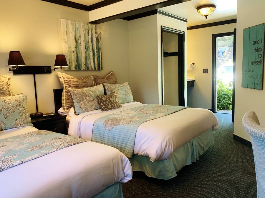 A hotel room with two beds, a large window, a mirror, and a wall with a quote.