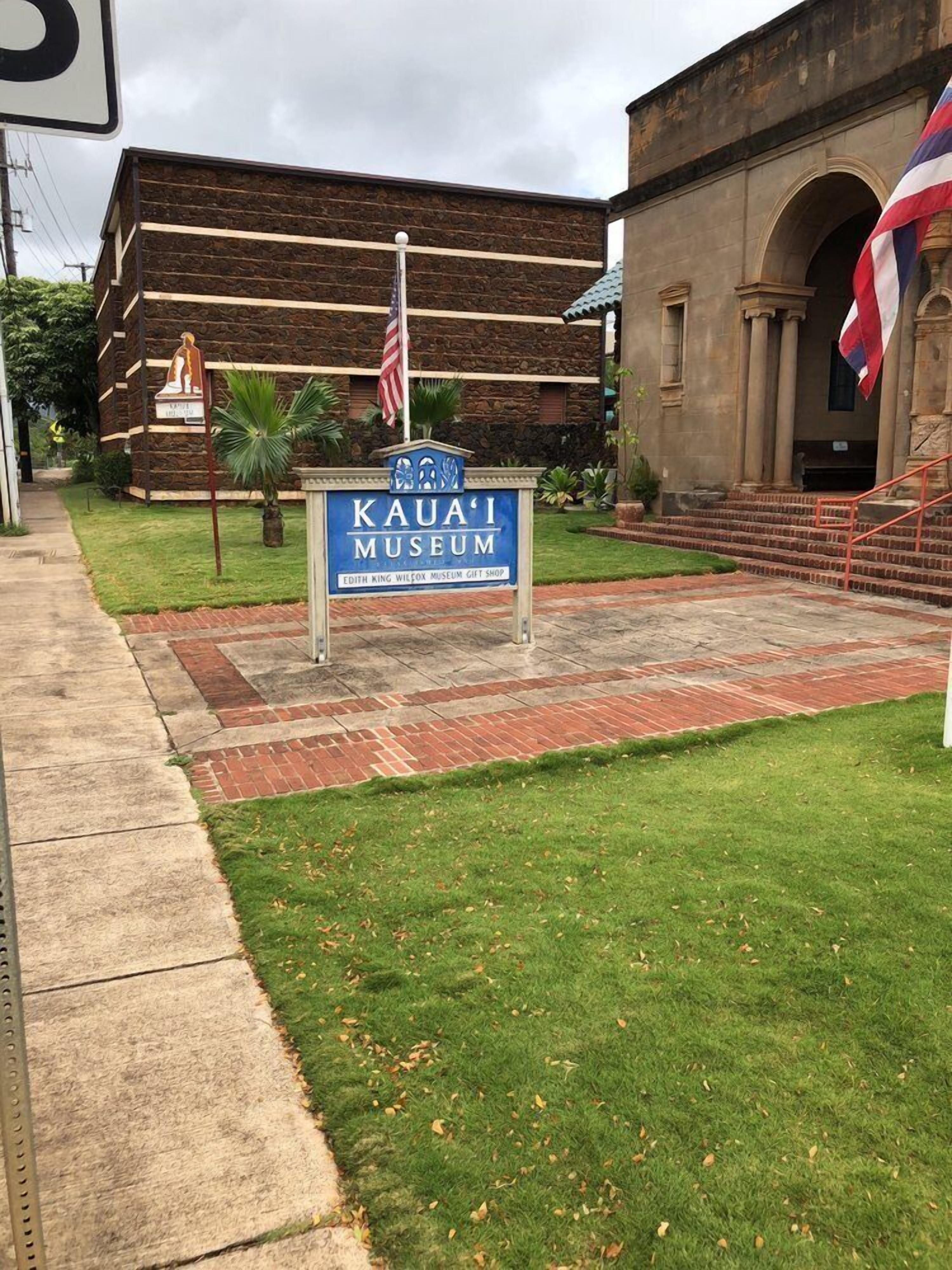 Een bord voor het Kaua'i Museum met een souvenirwinkel, een gebouw van steen en een Amerikaanse vlag.