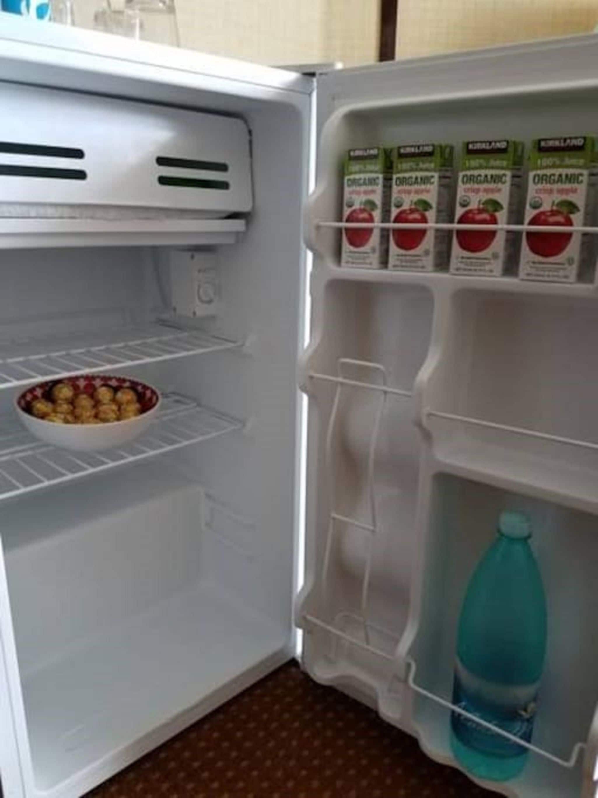 Un refrigerador abierto con un bol de fruta en el estante inferior, una botella de agua en el repisa de la puerta y cajas de jugo orgánico en el estante superior.