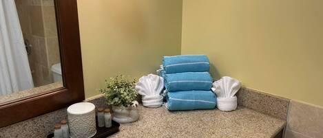 A bathroom with a granite countertop, a sink, a mirror, a potted plant, and neatly folded towels.